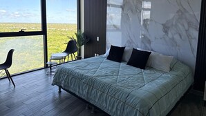 Un dormitorio con una cama grande, vistas al paisaje, una planta en maceta y una mesita.