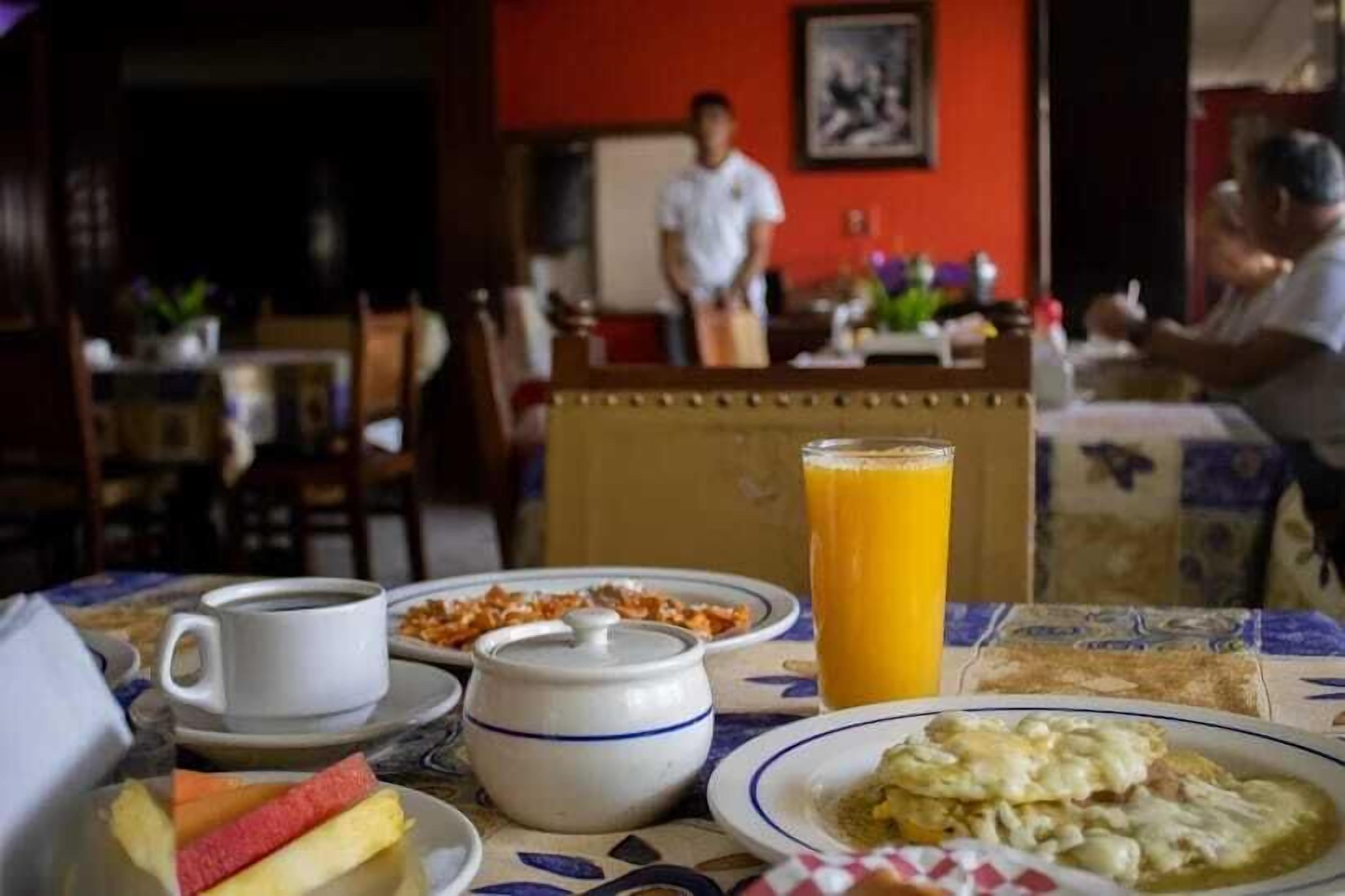 A breakfast setting with a coffee cup, fruit, a tall glass of orange juice, and a plate of eggs.