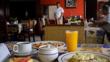 A breakfast setting with a coffee cup, fruit, a tall glass of orange juice, and a plate of eggs.