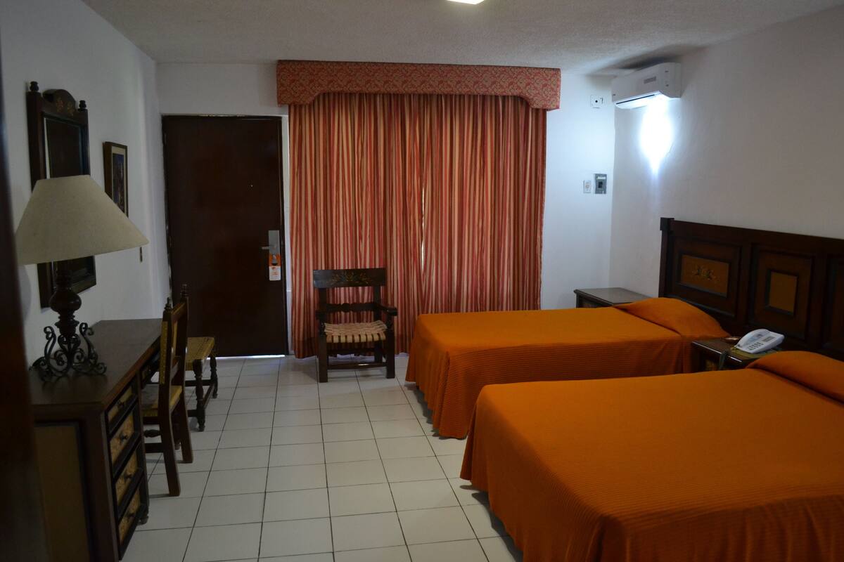 Una habitación de hotel con dos camas, un escritorio, una silla, una lámpara y un teléfono.