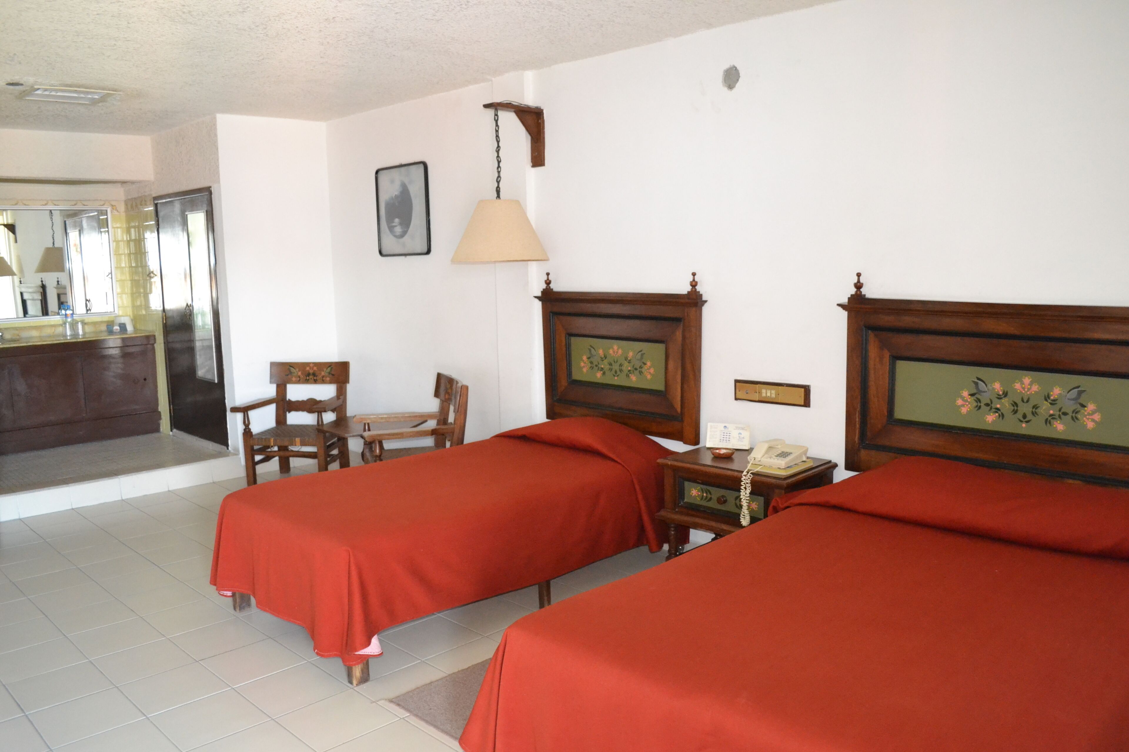 Une chambre d’hôtel avec deux lits, une table de chevet en bois, une chaise, un bureau, une lampe et un miroir.