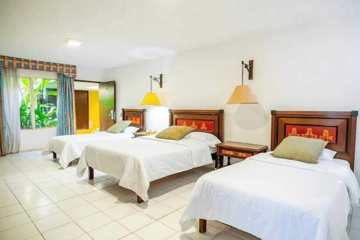 Habitación de hotel con tres camas individuales, una mesita y una lámpara.