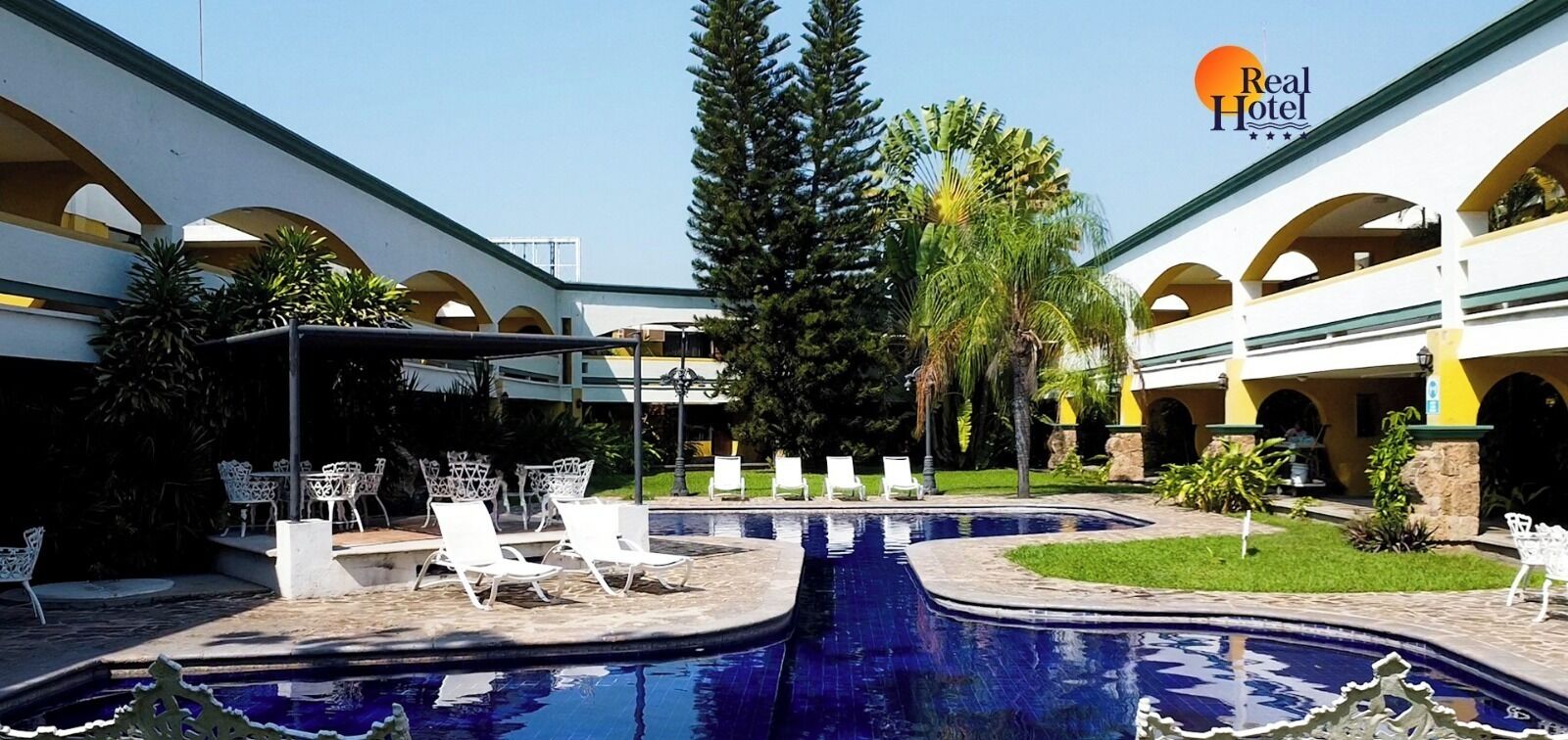 Un patio de hotel con piscina, sillones de descanso y una zona de estar cubierta.