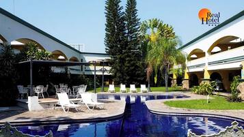 Un patio de hotel con piscina, sillones de descanso y una zona de estar cubierta.
