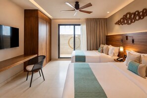 Habitación de hotel con televisión, escritorio, dos camas, ventilador de techo y un ventanal grande.