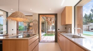 A modern kitchen with wooden cabinets, a large island, and a view of the outdoor pool area. - New 362 m² fully equipped villa, located in Ramatuelle (Ramatuelle)