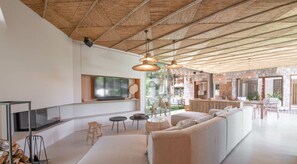 A modern living room with a large TV, wooden ceiling, and a dining area with a stone wall. - New 362 m² fully equipped villa, located in Ramatuelle (Ramatuelle)