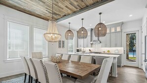 Une cuisine moderne dotée d’un îlot central en bois, de luminaires suspendus et d’un coin repas avec des chaises rembourrées.