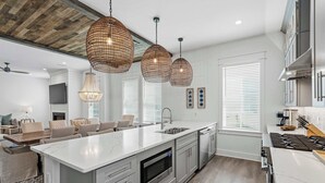 Une cuisine moderne dotée d’un grand îlot central, d’appareils électroménagers en acier inoxydable et de luminaires suspendus.