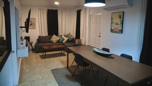 Uma sala de estar com sofá, mesa de jantar e televisão.