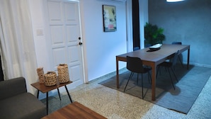 Uma sala de jantar com mesa, cadeiras, luminária pendente, porta e ar-condicionado fixado na parede.