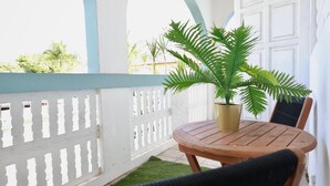 Uma mesa de madeira redonda com uma planta em vaso, cerca branca de piquete e uma porta branca ao fundo.