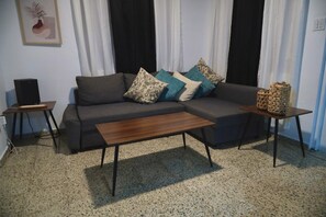 Una sala de estar con un sofá, una mesa de centro, un altavoz y una cesta tejida sobre una mesita auxiliar.