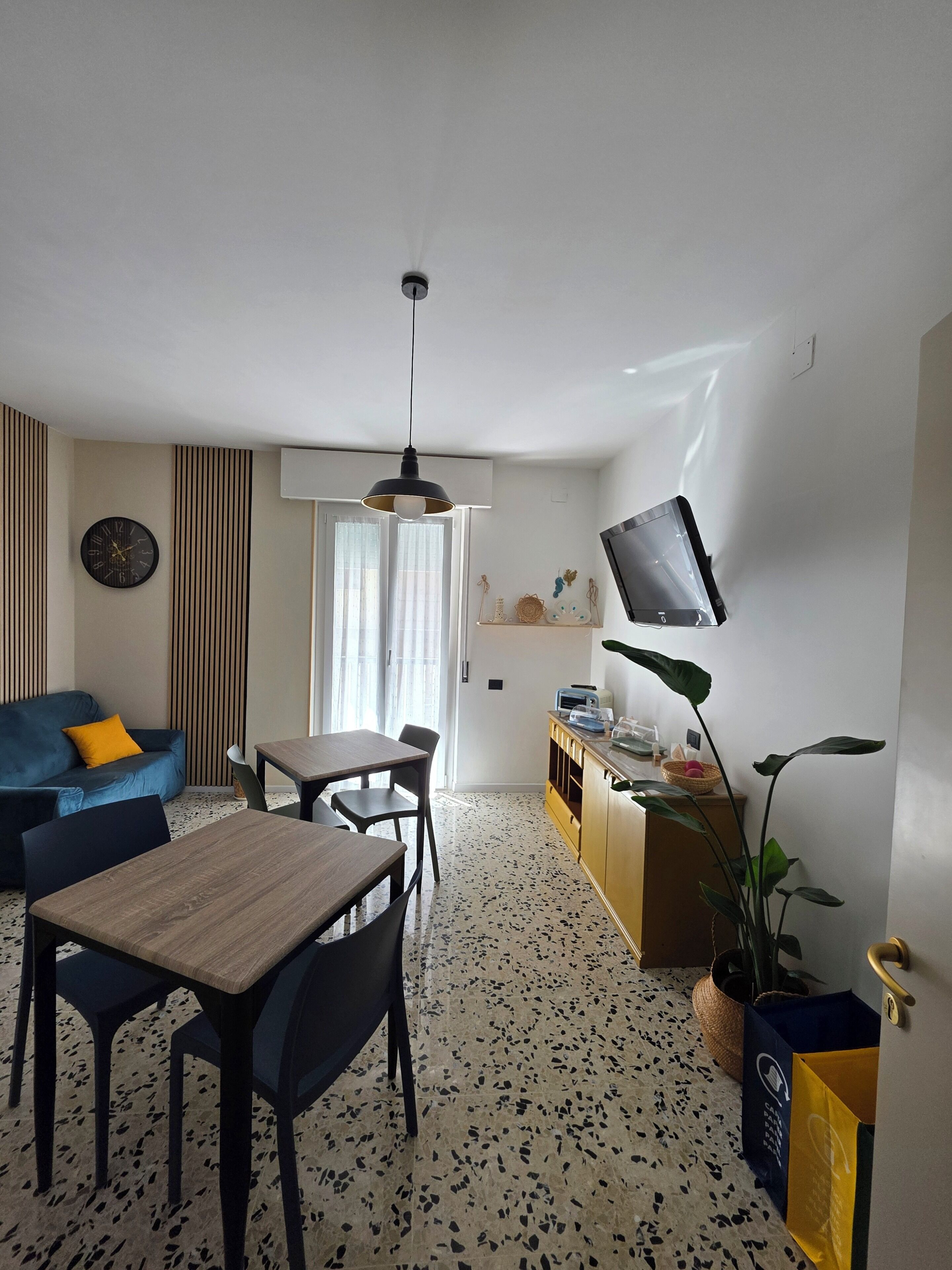 Ein modernes Wohnzimmer mit einer Couch, einem Esstisch, Stühlen, einem Fernseher und einer Pflanze.