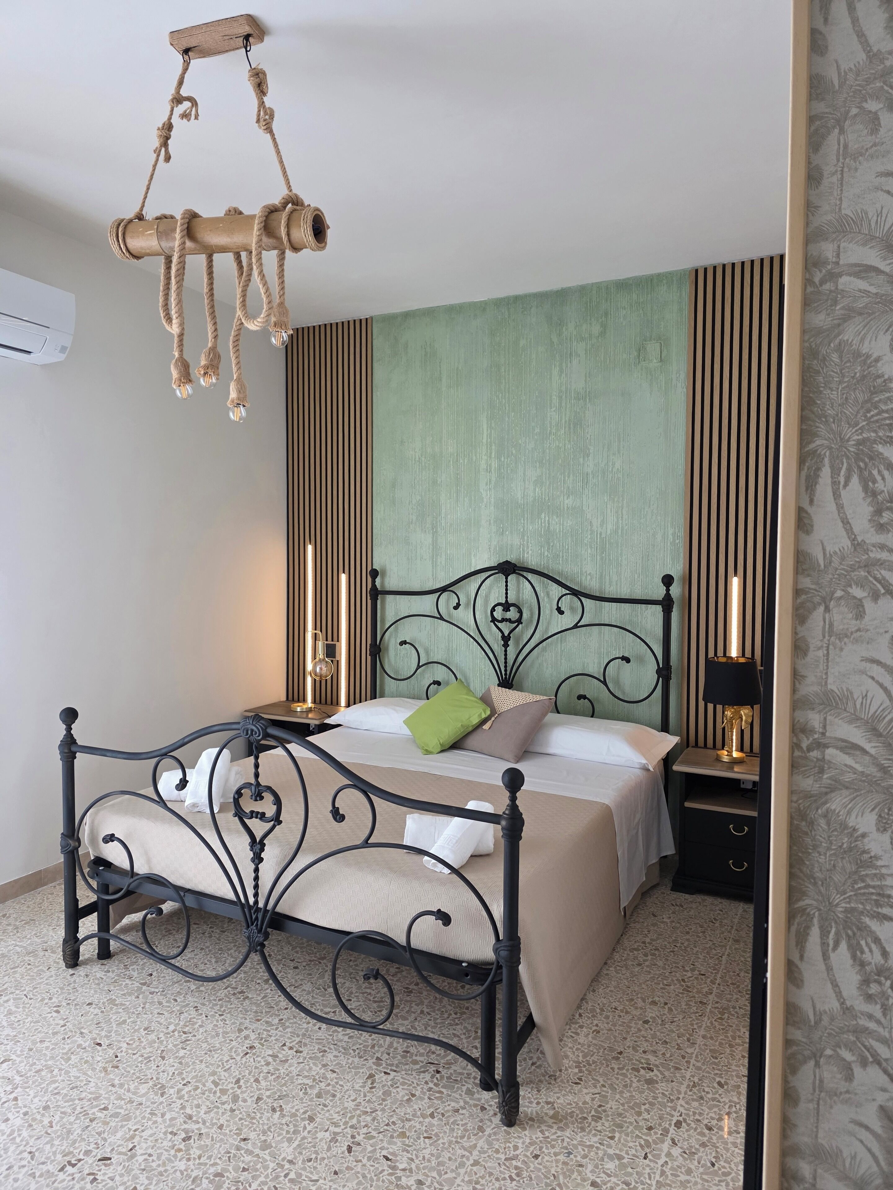 Une chambre à coucher comprenant un lit, des tables de chevet, un luminaire suspendu et un climatiseur fixé au mur.