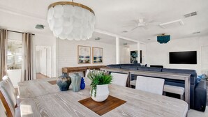 A modern kitchen with a dining area, white walls, and a large wooden table. - Fire & Oaks Estate (Tybee Island)