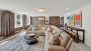 A modern living room with a sectional sofa, a round coffee table, and a dining area with bar stools. - Fire & Oaks Estate (Tybee Island)