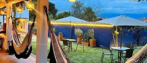 A covered outdoor area with hammocks, tables, chairs, and potted plants.