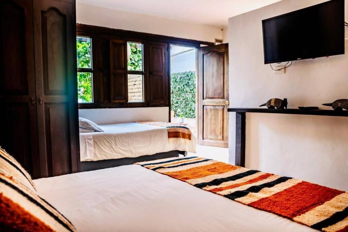 A bedroom with two beds, a television, and a window with a view of greenery.