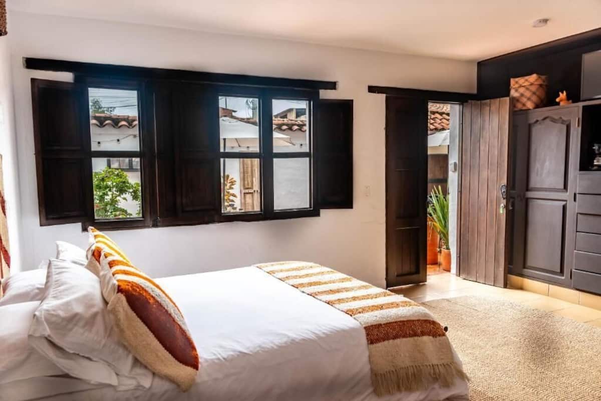 A bedroom with a bed, a window with shutters, a door, and a view of the outside.