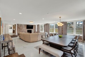 A spacious living area with a brick fireplace, a large dining table, and a comfortable sofa. - Fire & Oaks - The Ember Villa (Tybee Island)