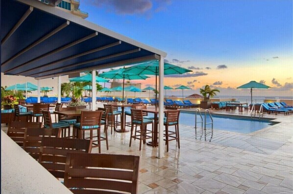 Un espace aménagé au bord de la piscine, avec des chaises longues, des parasols et une vue sur l’océan.