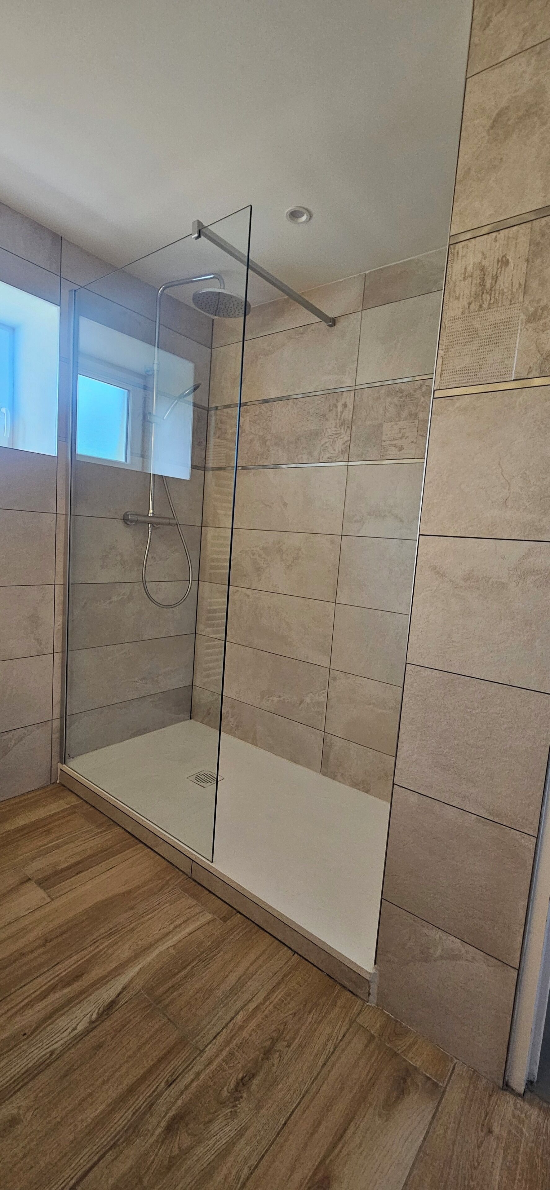 Um banheiro moderno com chuveiro em box de vidro, paredes revestidas com azulejos e piso de madeira.