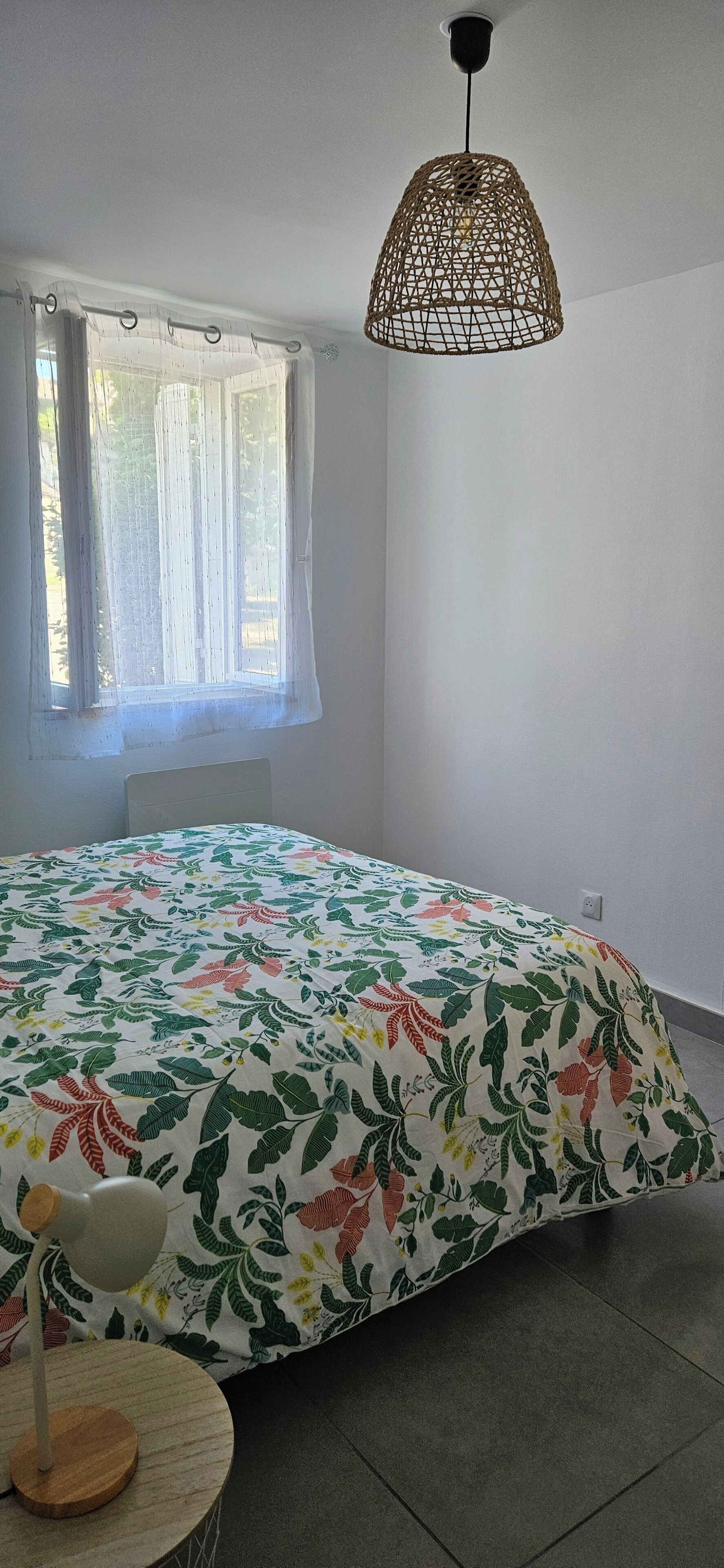 Et soveværelse med en seng, et vindue med gardiner, en hængende lampe og et rundt bord med en lampe.