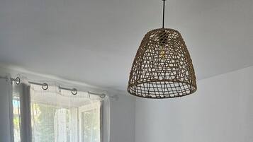 Een slaapkamer met een bed, een raam met gordijnen, een hanglamp en een klein, rond tafeltje met een lamp.