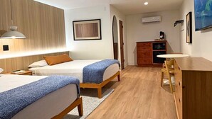Habitación de hotel con dos camas, un escritorio, una silla, un ventilador de techo y un ventanal grande.