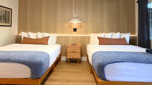 Habitación de hotel con dos camas, una mesita de noche, una lámpara de pared y un cuadro en la pared.