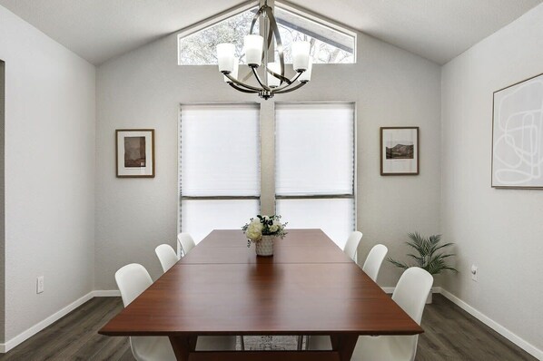 A dining room with a wooden table, white chairs, a chandelier, and framed pictures on the walls. - Candleridge Casa - Newly Remodeled 4-bd Hidden Gem (Fort Worth)