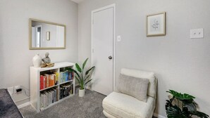 A clean, minimalistic entryway with a white console table holding books and decorative items, a white armchair, and a door with a small framed picture above it. - Candleridge Casa - Newly Remodeled 4-bd Hidden Gem (Fort Worth)