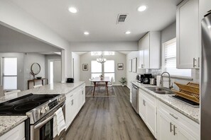 Una cocina moderna con armarios blancos, una isla central y un comedor con candelabro.
