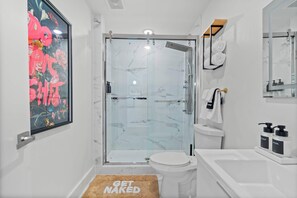 Ein modernes Badezimmer mit Duschkabine aus Glas, einer weißen Toilette, einem weißen Waschbecken und einem großen Spiegel.