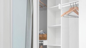 En walk-in-garderob med öppna dörrar, en klädstång och en korg av rotting.