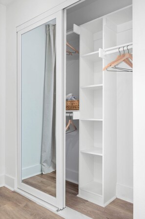 Ein begehbarer Kleiderschrank mit offenen Türen, einer Kleiderstange und einem Korbwäscheschrank.