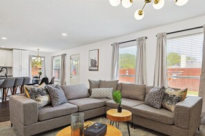 A modern living room with a sectional sofa, a round coffee table, and a dining area in the background. - Modern Comforts & Classic Charm w Pool, 5BD (Fort Worth)