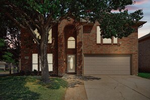 A two-story brick house with a garage, a tree in front, and a well-maintained lawn. - Modern Comforts & Classic Charm w Pool, 5BD (Fort Worth)