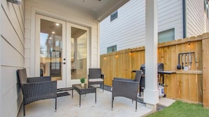Une terrasse couverte, meublée de mobilier en osier, avec un barbecue et une clôture en bois.