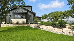 A modern house with a stone foundation, a well-maintained lawn, and a view of the water. - Heavenly Retreat 5bd/5.5ba of Waterfront living (Gainesville)