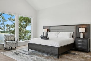 A bedroom with a large bed, two bedside tables, a chair, and a view of the outdoors. - Heavenly Retreat 5bd/5.5ba of Waterfront living (Gainesville)