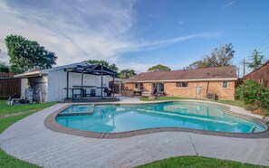 Ein Garten mit Schwimmbad, überdachter Terrasse und einem Ziegelhaus.