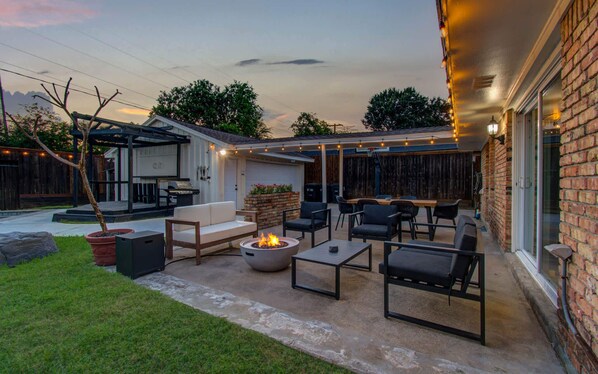 Eine Terrasse im Freien mit Feuerstelle, Sitzgelegenheiten und Lichterketten.