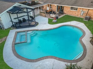 A backyard with a swimming pool, a covered patio, and a brick house. - 4-bd Central Location w Pool, Patio, Firepit (Houston)
