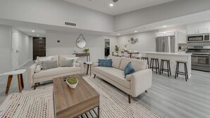 Ein modernes Wohnzimmer mit einer Couch, einem Couchtisch und einer Küchenzeile mit Kühlschrank, Mikrowelle und Barhocker.