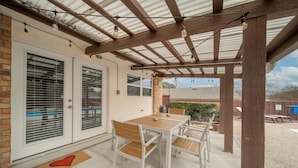 Eine überdachte Terrasse mit Tisch und Stühlen, einer Backsteinmauer und einer Metallkonstruktion als Dach.