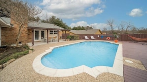 Ein Garten mit Swimmingpool, einer Holzterrasse und einem eingezäunten Bereich mit Liegestühlen.