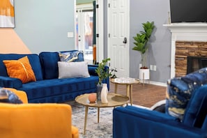 A living room with a blue sofa, a small round table, and a fireplace. - Best of Saginaw 4bd/2ba w Pool, Pool Table & BBQ (Fort Worth)