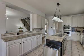 A modern kitchen with white cabinets, granite countertops, stainless steel appliances, and a central island. - Spacious & Cozy Texas Gem With Private Pool (Plano)
